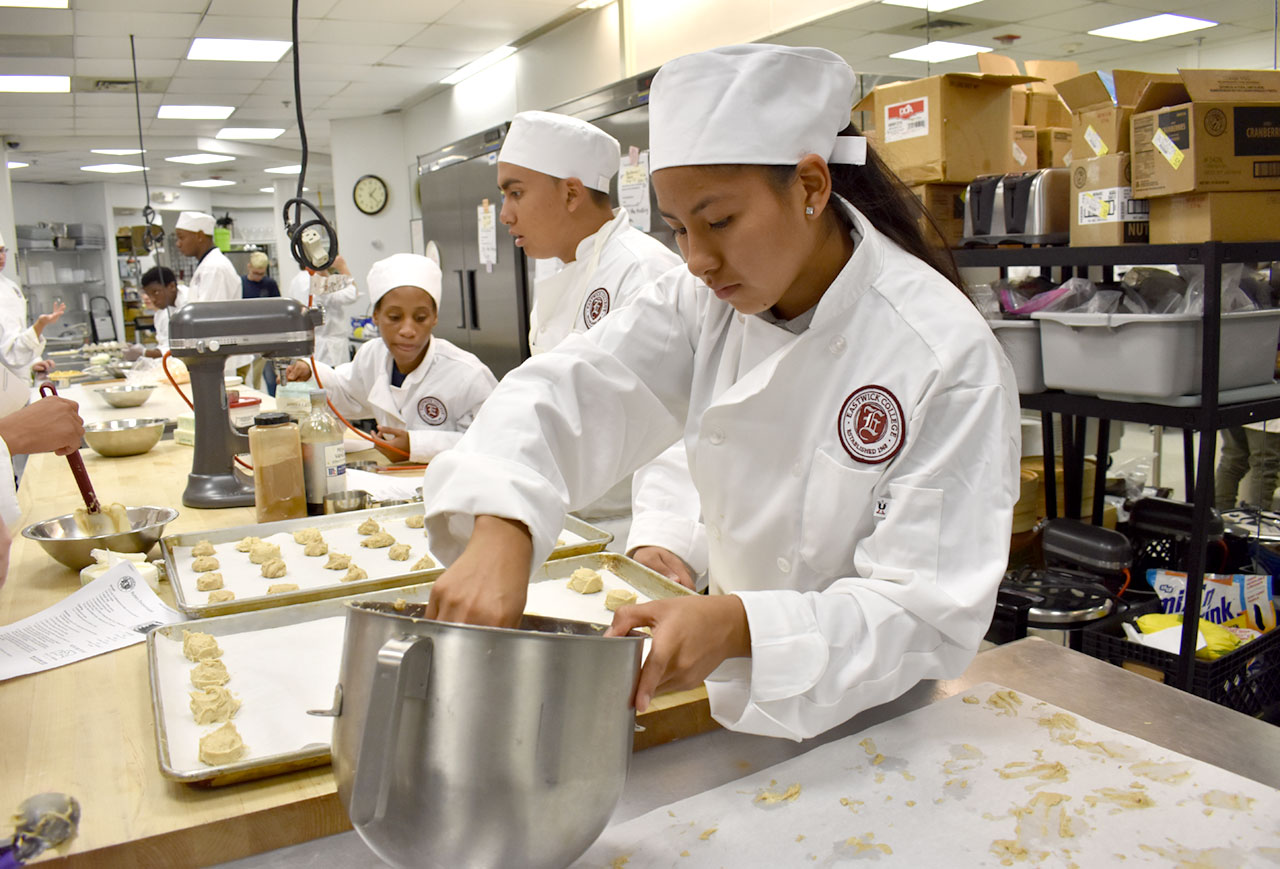 Culinary program students measure out balls of dough onto baking sheet