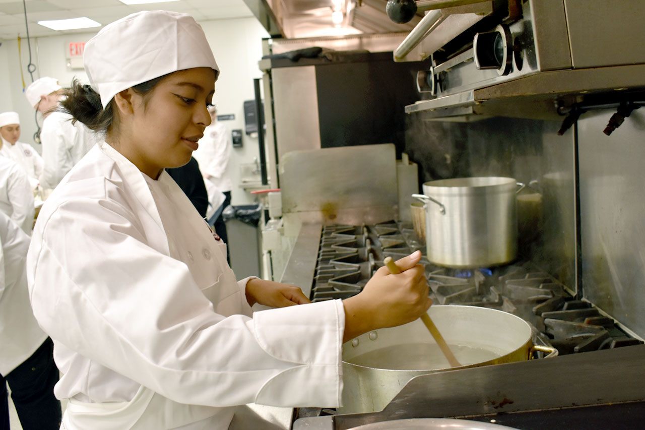 Culinary program student stirs pot in kitchen