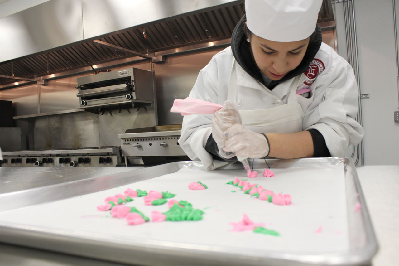 Culinary program student pipes flowers made of frosting onto baking sheet