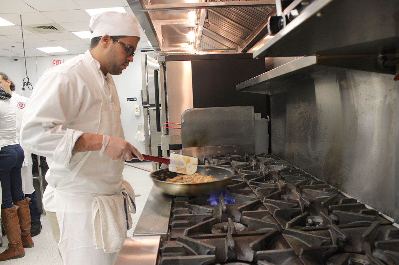 Culinary arts student stands in front of gas stove and stirs ingredients in pan