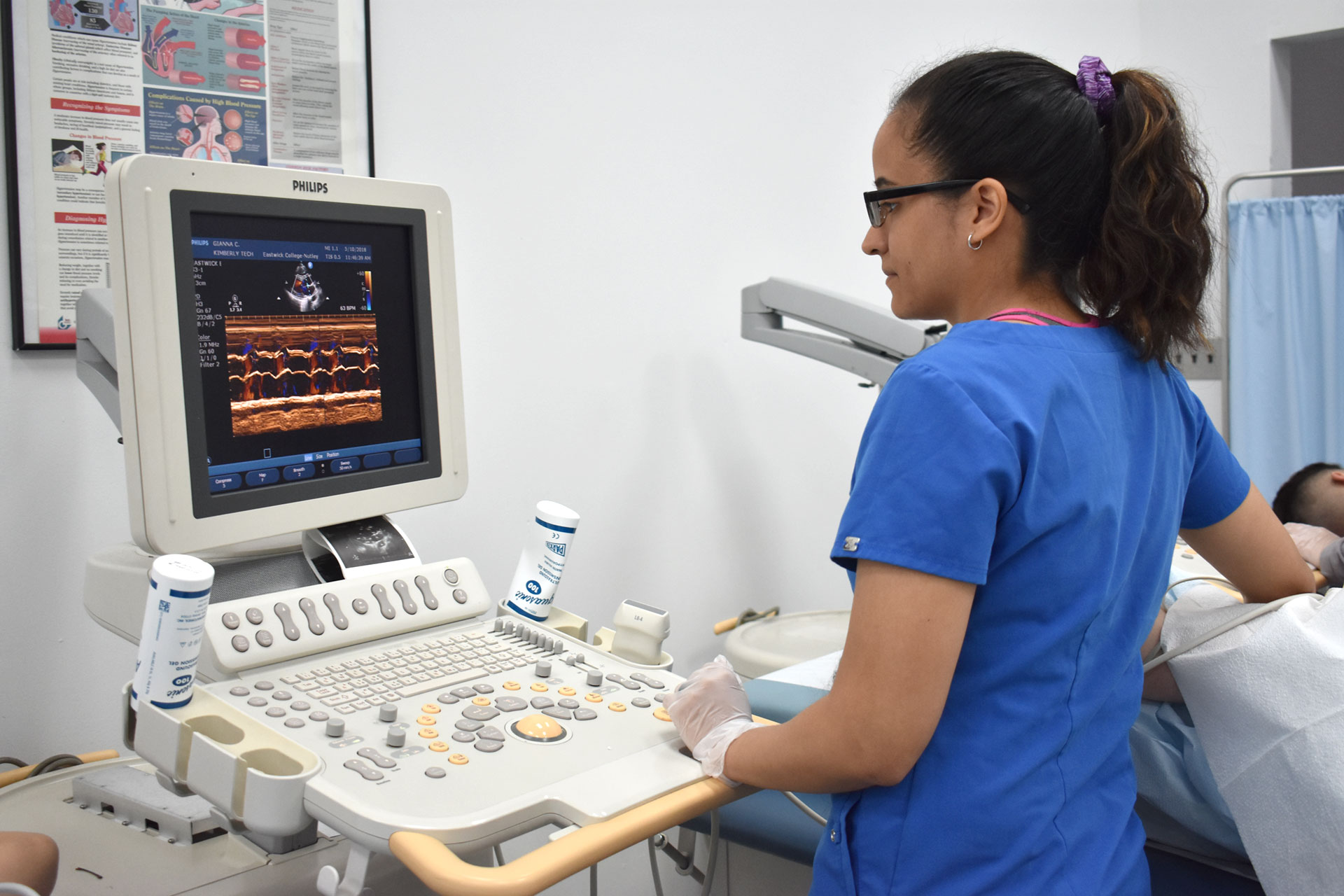 Sonography student practices observing ultrasound machine on fellow student