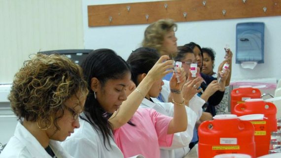 medical students practice taking liquid from a bottle using a syringe